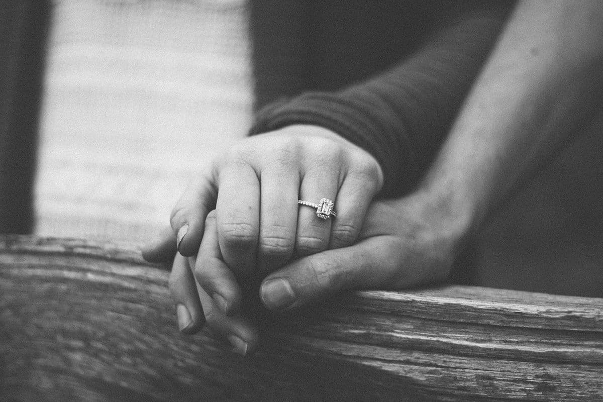 Black-and-white photo of a couple holding hands, her engagement ring visible